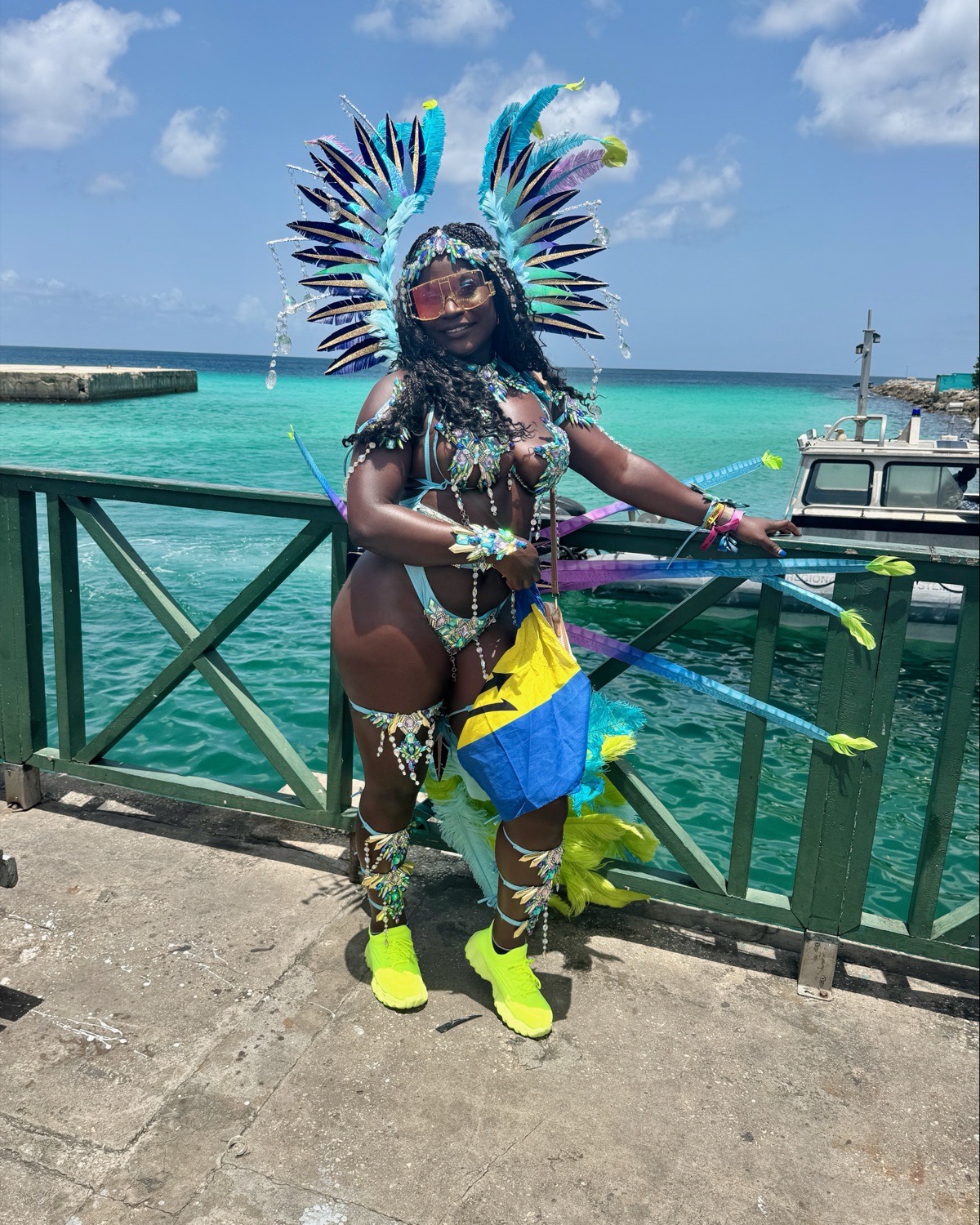Stephanie in a blue and yellow Crop Over costume on a pier, turquoise water behind her.